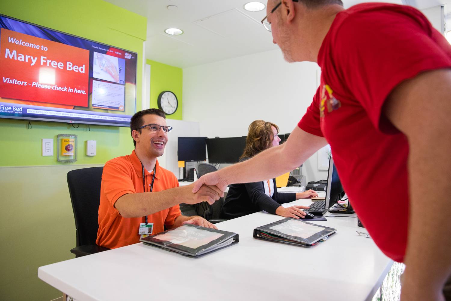 volunteer is seated at a check-in table and greets a guest